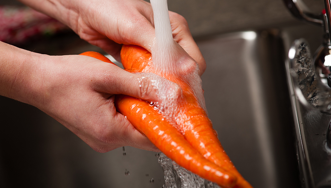 Person washing carrots in running water.