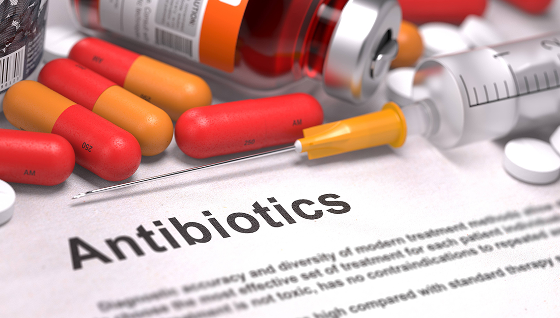 The word "antibiotics" on a piece a paper next to a syringe and pills.