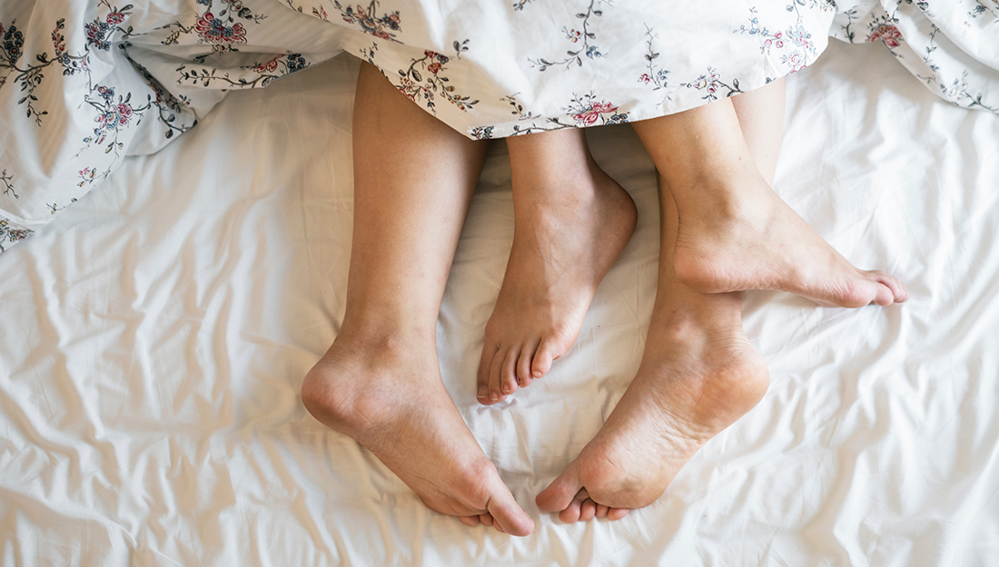 Two pairs of feet peeking out from beneath a blanket on a bed.