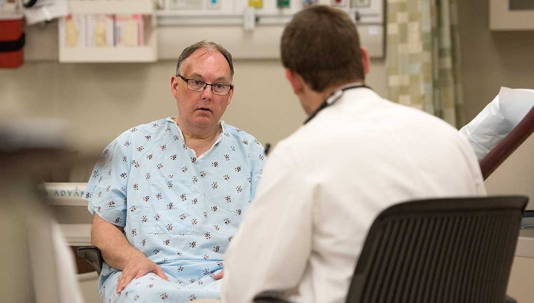 Man in a hospital gown speaking with a physician in a white coat about his pain levels