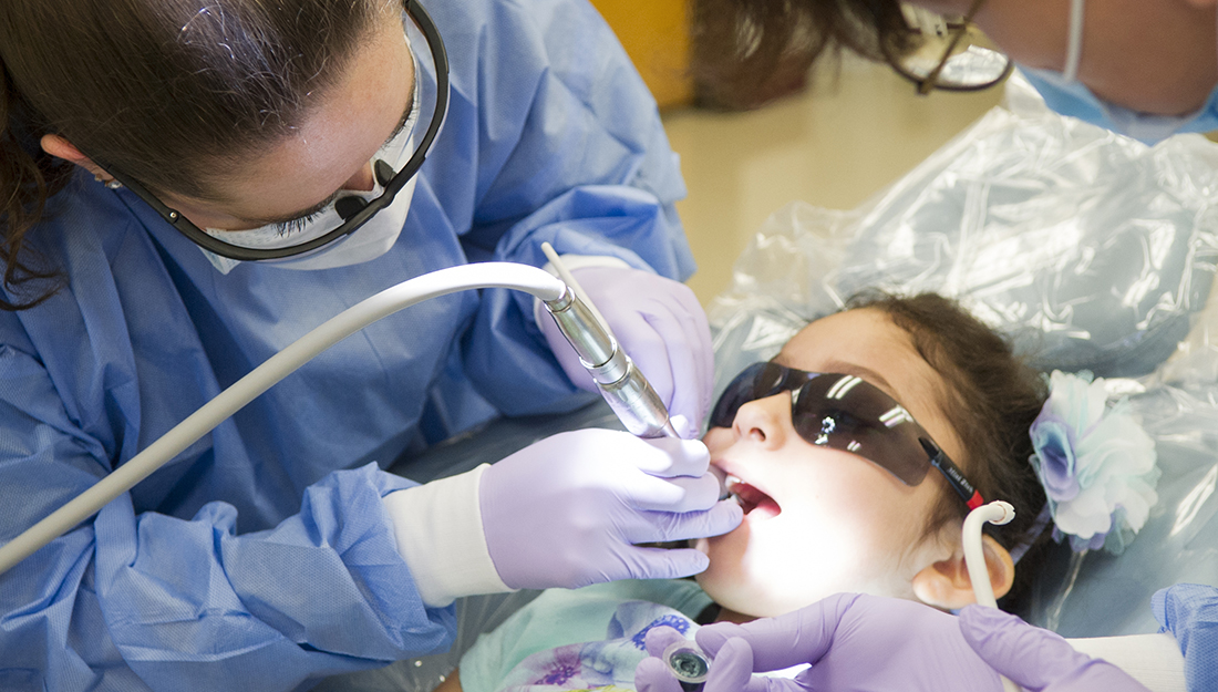 Give Kids a Smile - A dentistry professional performs a dental procedure on a child.