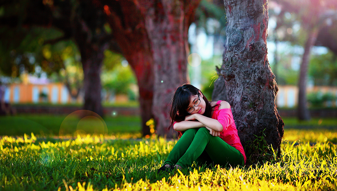 Mental Health - A girl sitting in the grass under a tree with her head resting on her knees