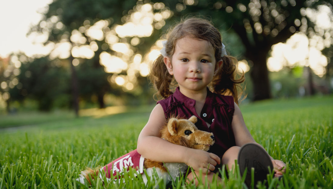 Childhood development_Child development_A young girl is sitting in grass holding a stuffed animal