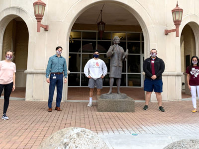 five students pose in front of Rangel College of Pharmacy building wearing hand-sewn face masks