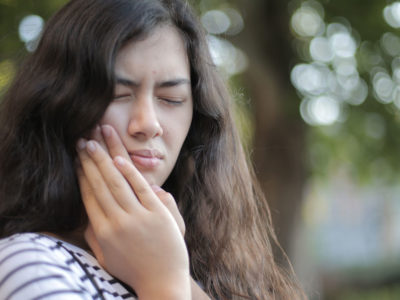 A woman with long brown hair clenches her jaw with eyes closed as if in pain
