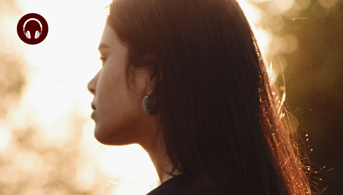 Backlit side view of woman with dark hair standing outside with eyes closed during sunset
