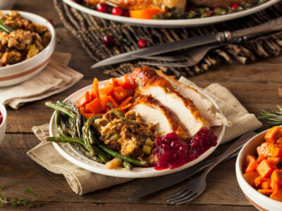 table full of Thanksgiving food, plate of turkey, stuffing, sweet potatoes, asparagus and cranberry sauce