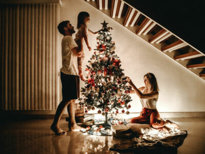 family of three decorates a Christmas tree in their home