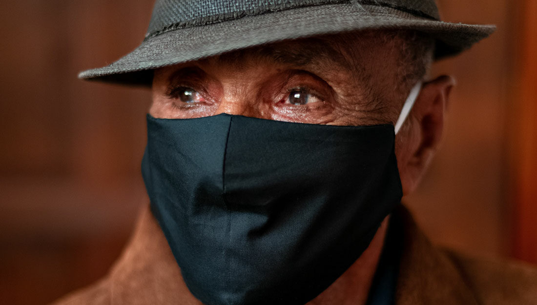 older man wearing a hat and face covering