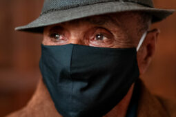 older man wearing a hat and face covering