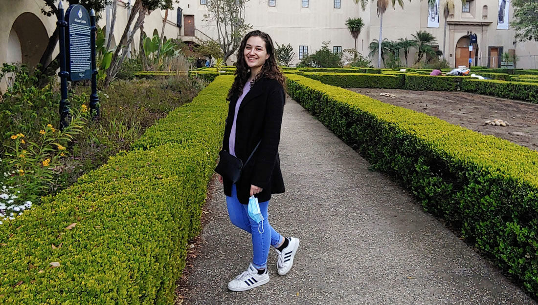 Lacy Failla stands on a hedge-lined sidewalk in a park