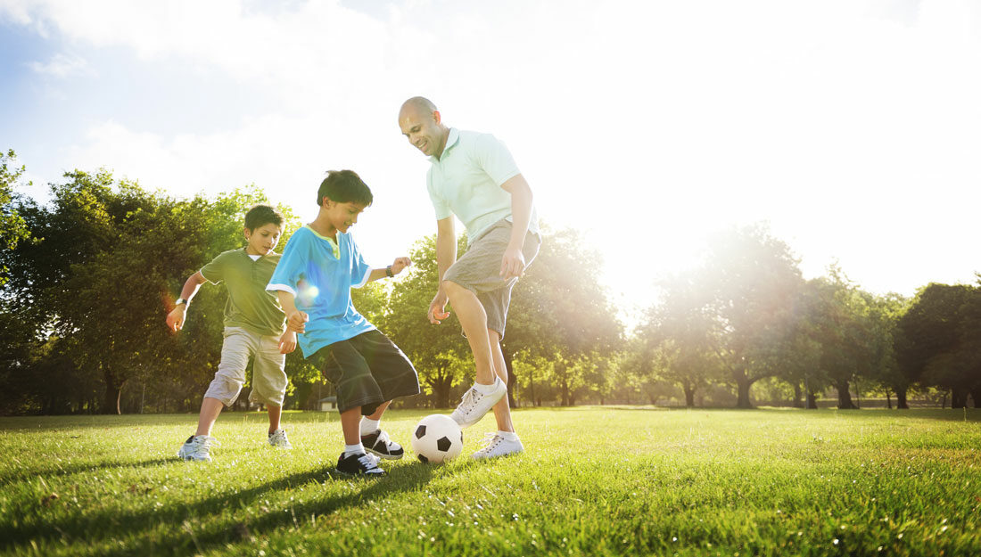 father kicks soccer ball with two sons