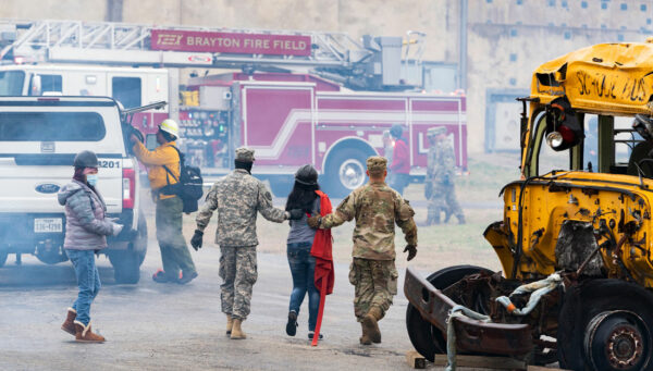 students walk together through Brayton Fire Field as smoke billows through