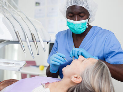 Mature female patient sitting in dental chair. Dental hygienist is treating female patient
